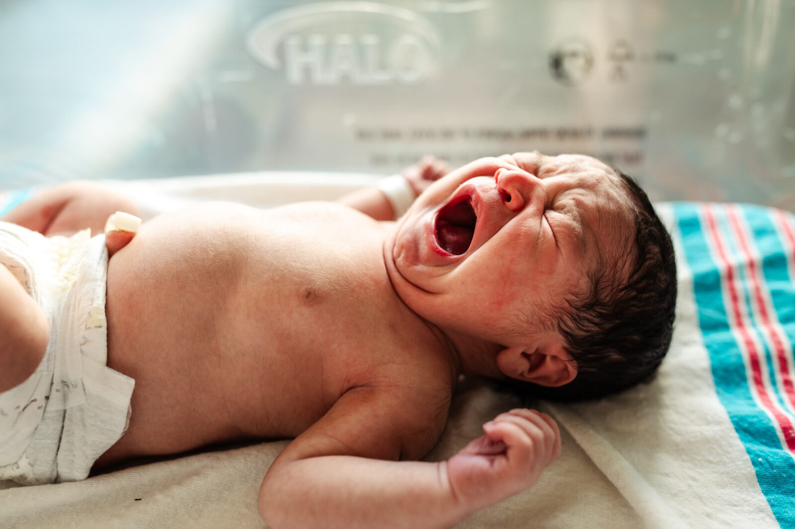 A newborn yawns and stretches inside of their hospital bassinet