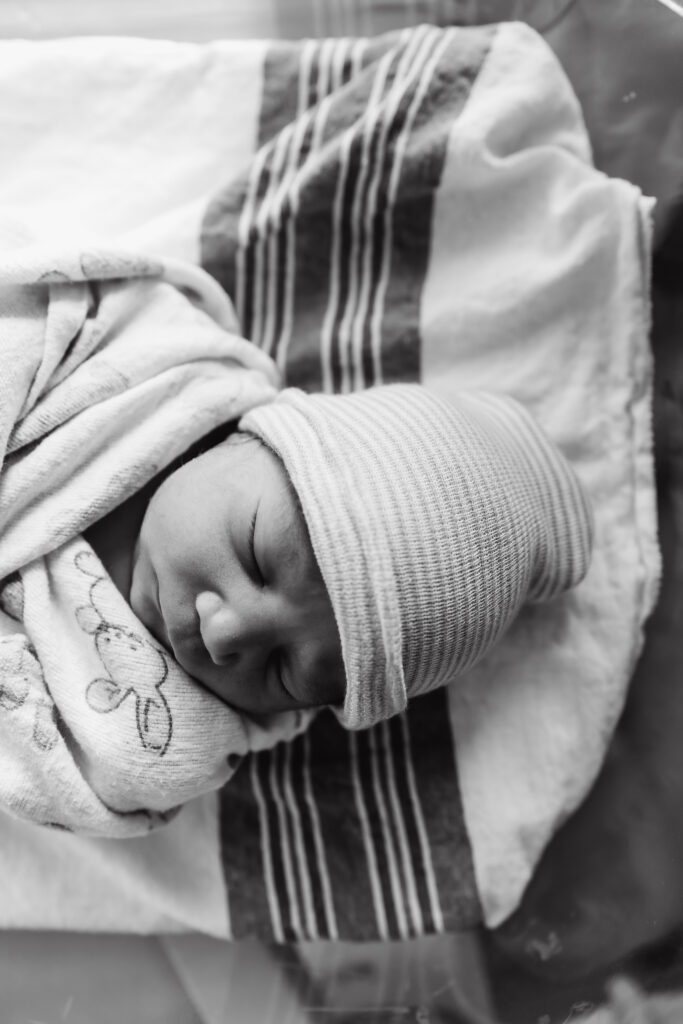 A sweet new baby sleeps in a hospital bassinet in black and white.  Mom will need to see a pelvic floor therapist after having her c-section. 