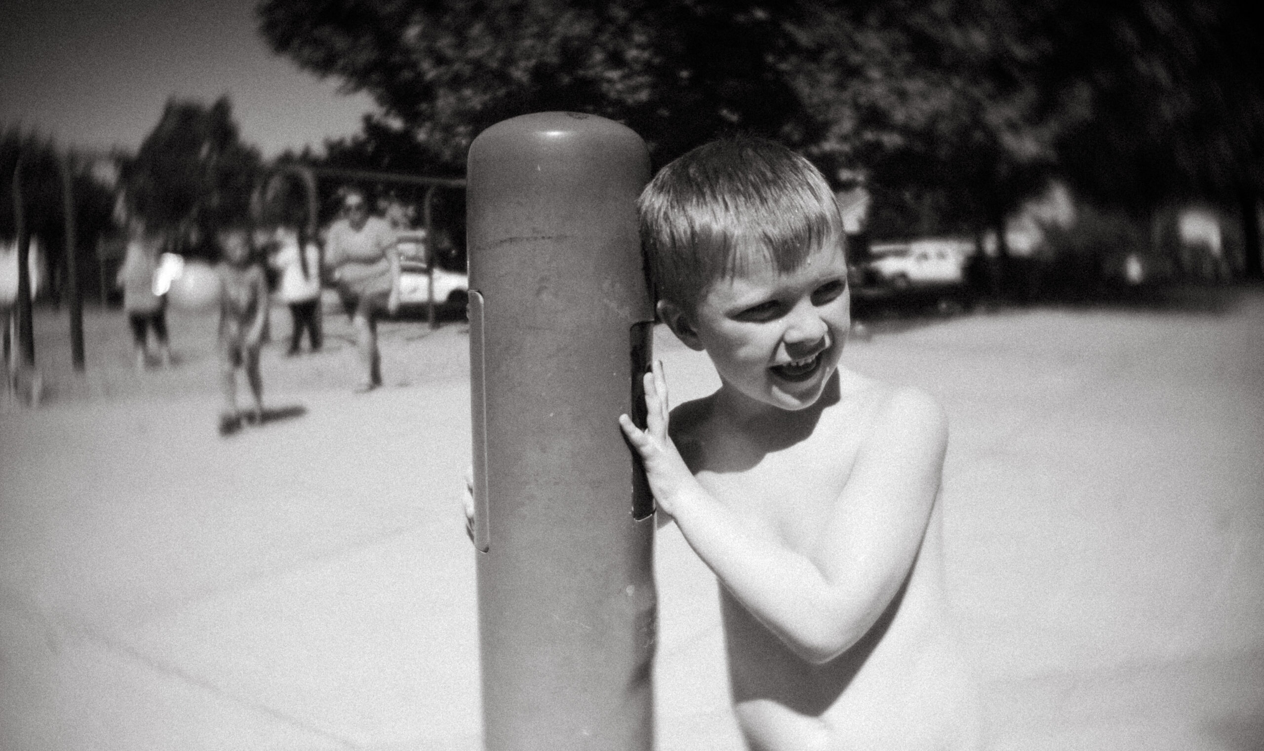 little boy standing in a park next to a water feature and smiling