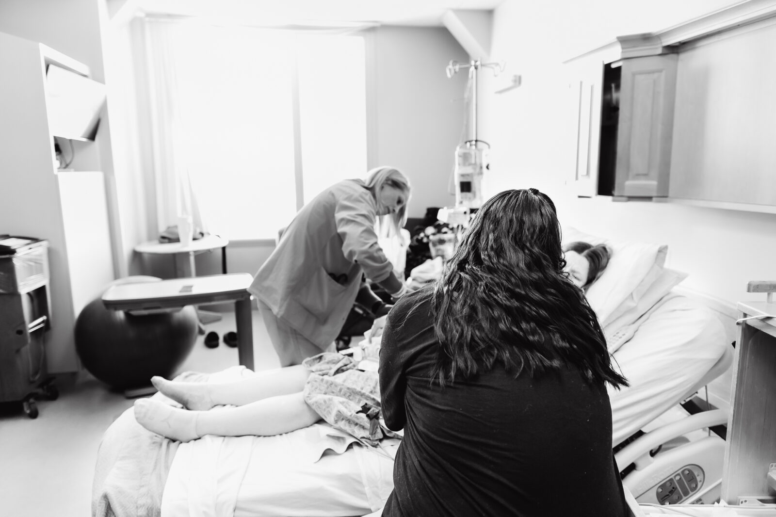 A young woman sits in a hospital bed while her friend offers her comfort, representing miscarriage support