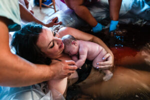 A happy mom who has listened to many pregnancy podcasts clings to her new baby in the birthing tub, smiling and relieved that she has birthed her baby