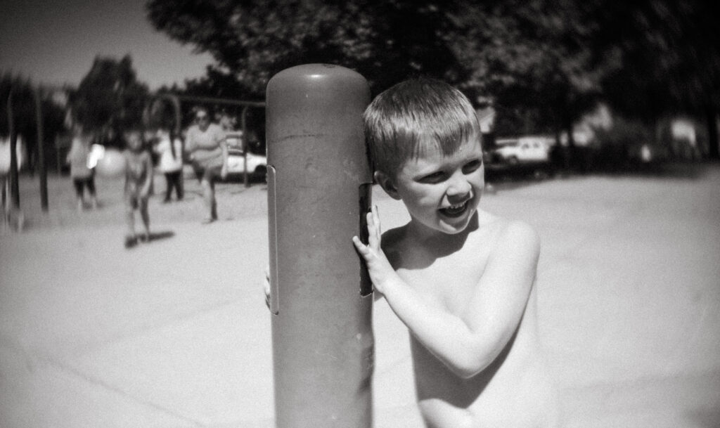 a little boy stands by a pole in a Modesto park waiting to play on the splash-pad. Love of water is one of the signs of autism in young children. 