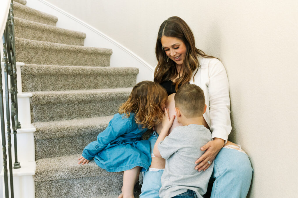 A mom holds two of her kids as they kiss her pregnant belly, and this sweet family would have so much fun joining a mommy and me class in modesto. 