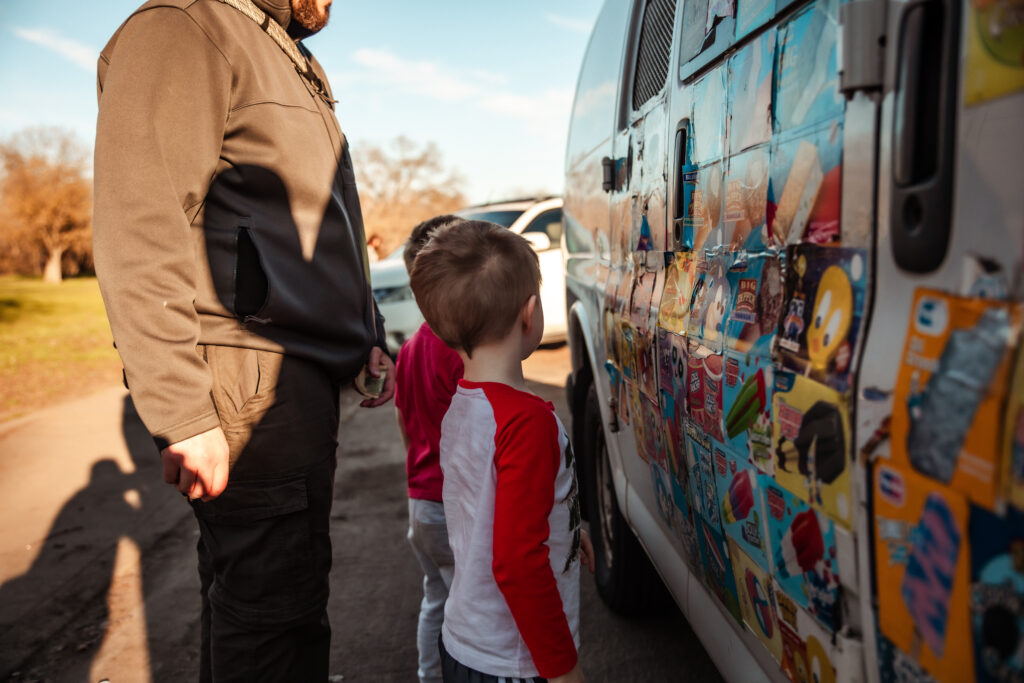 Two little boys stand in front of an ice cream truck at a park in modesto, california, waiting for their turn