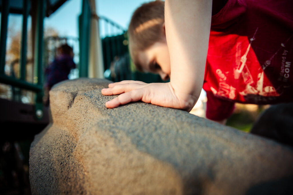 a little boy climbs on a rock-like playstructure in one of the many playgrounds in modesto, CA