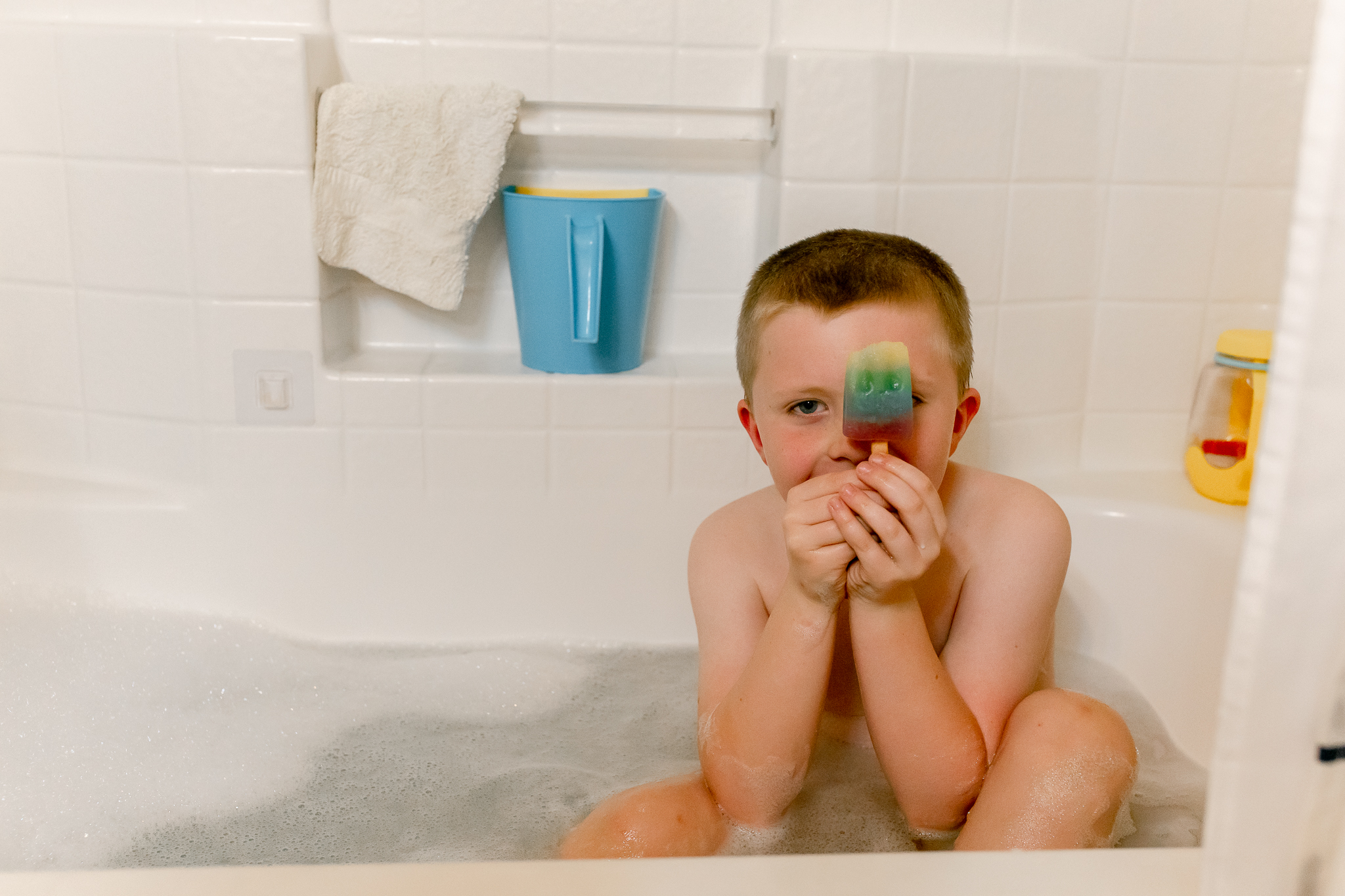 A little boy sits in a bathtub with a popsicle. HIs mom should take him to one of Modesto's parks with water to keep him cool in the Summer!
